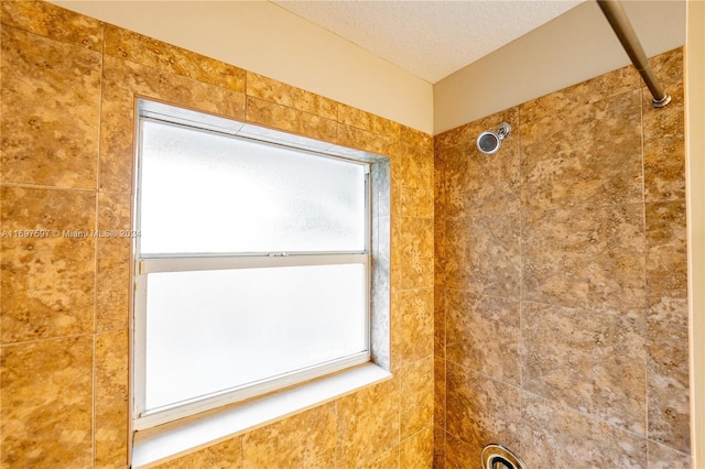 bathroom with a tile shower, a textured ceiling, and a wealth of natural light