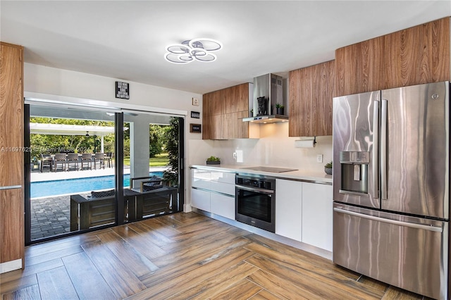 kitchen featuring white cabinets, light parquet flooring, stainless steel appliances, and wall chimney range hood