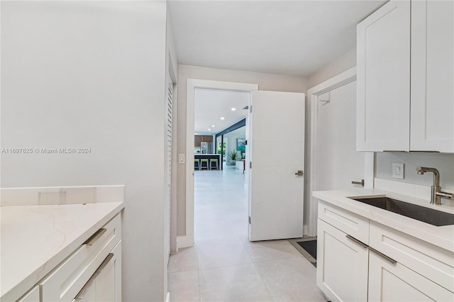 kitchen featuring white cabinets, light stone counters, light tile patterned flooring, and sink