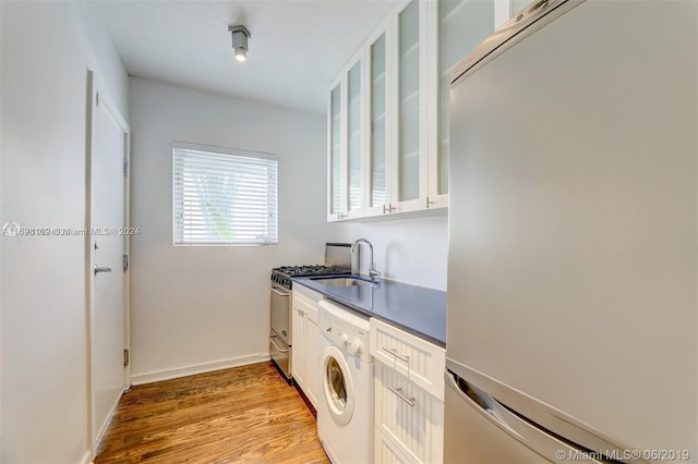 clothes washing area with washer / clothes dryer, light hardwood / wood-style flooring, and sink