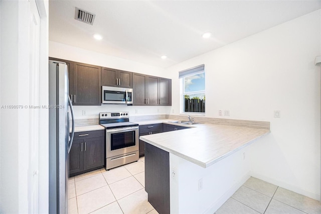 kitchen featuring kitchen peninsula, dark brown cabinets, stainless steel appliances, sink, and light tile patterned flooring