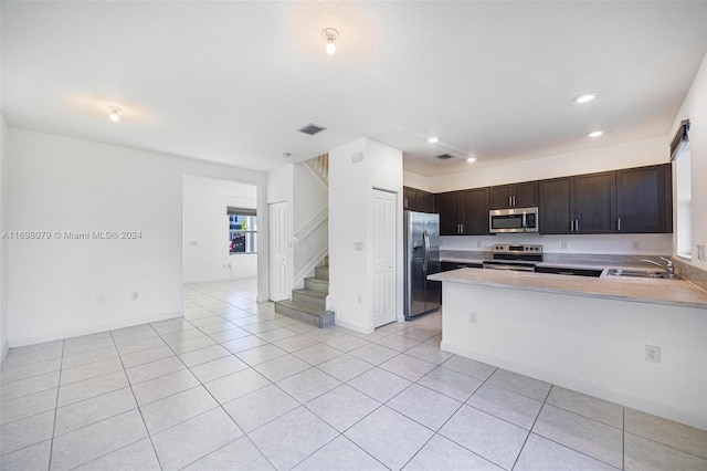 kitchen with sink, dark brown cabinetry, light tile patterned floors, kitchen peninsula, and stainless steel appliances