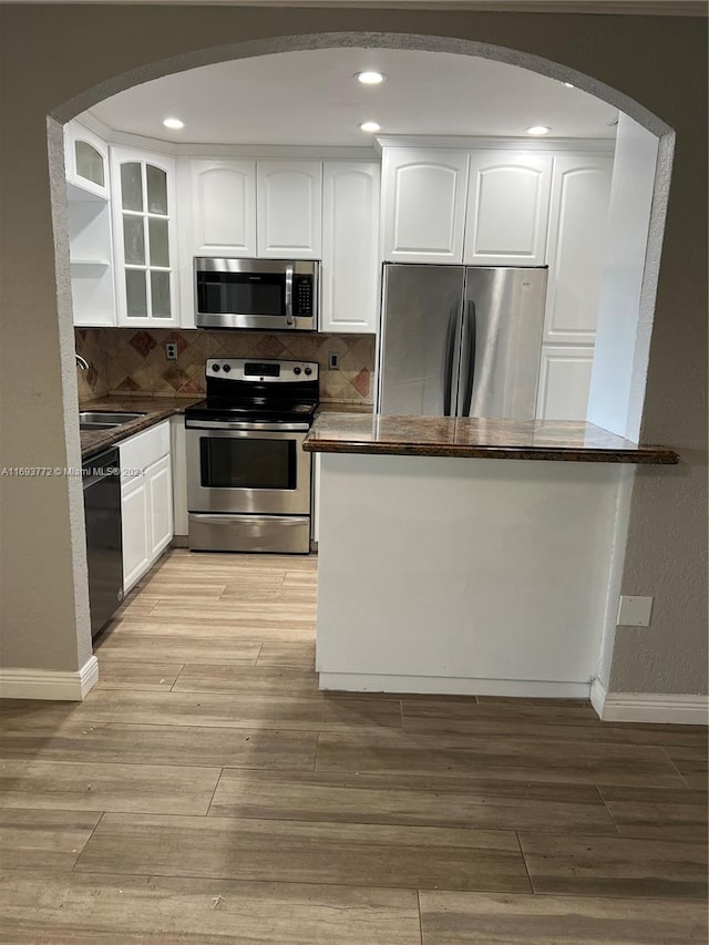 kitchen featuring white cabinetry, stainless steel appliances, backsplash, kitchen peninsula, and light hardwood / wood-style floors