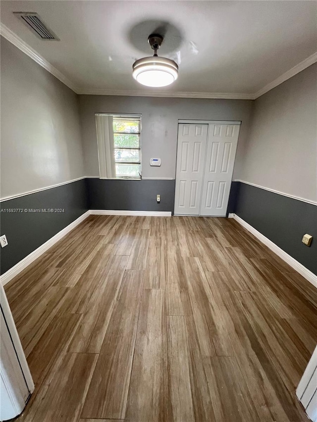 unfurnished bedroom with a closet, hardwood / wood-style floors, and ornamental molding