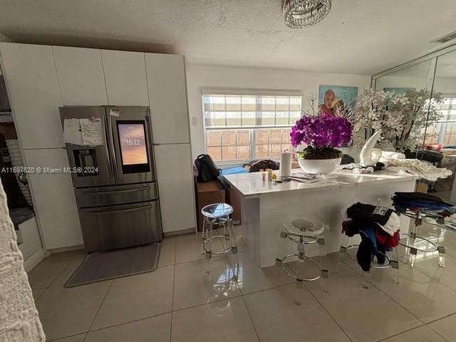 kitchen featuring stainless steel fridge, a textured ceiling, white cabinets, a breakfast bar area, and light tile patterned flooring