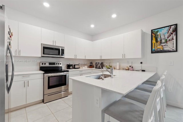 kitchen with kitchen peninsula, a breakfast bar, stainless steel appliances, sink, and white cabinetry