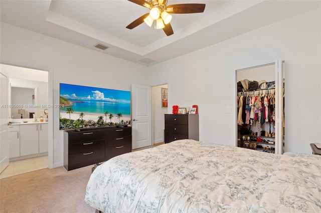 carpeted bedroom with a walk in closet, ensuite bath, ceiling fan, a tray ceiling, and a closet