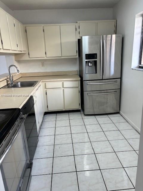 kitchen with stainless steel fridge with ice dispenser, light tile patterned floors, cream cabinets, and sink