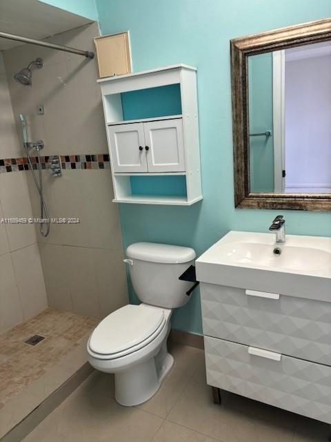 bathroom featuring tile patterned flooring, a tile shower, vanity, and toilet