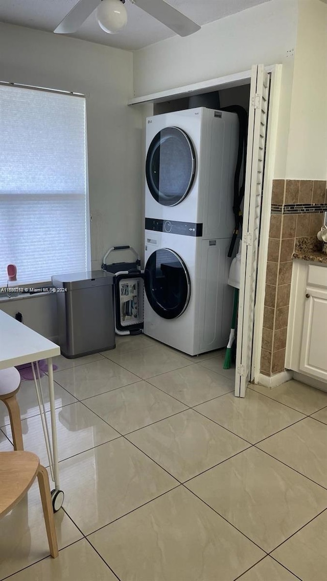 clothes washing area featuring light tile patterned flooring, stacked washer / dryer, and tile walls