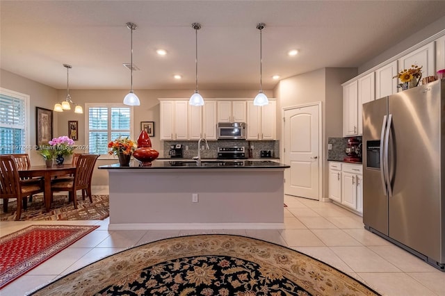 kitchen with white cabinets, decorative light fixtures, stainless steel appliances, and a kitchen island with sink