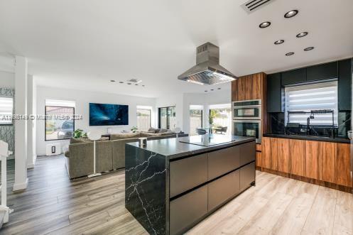 kitchen featuring a center island, black electric cooktop, double oven, range hood, and light hardwood / wood-style floors