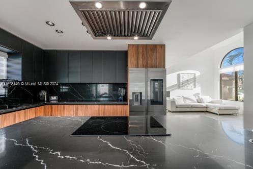 kitchen with stainless steel fridge, black electric stovetop, dark stone counters, and exhaust hood