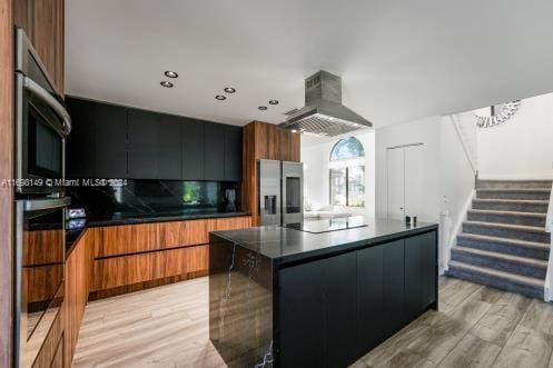 kitchen with a kitchen island, stainless steel appliances, range hood, and light hardwood / wood-style flooring