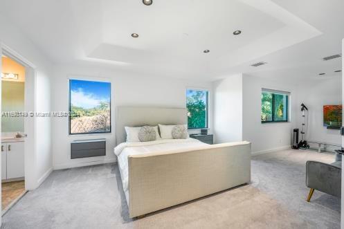 bedroom featuring ensuite bathroom, a tray ceiling, and light colored carpet