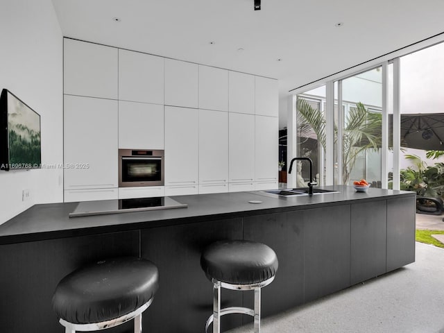 kitchen with stovetop, sink, white cabinetry, stainless steel oven, and a kitchen breakfast bar