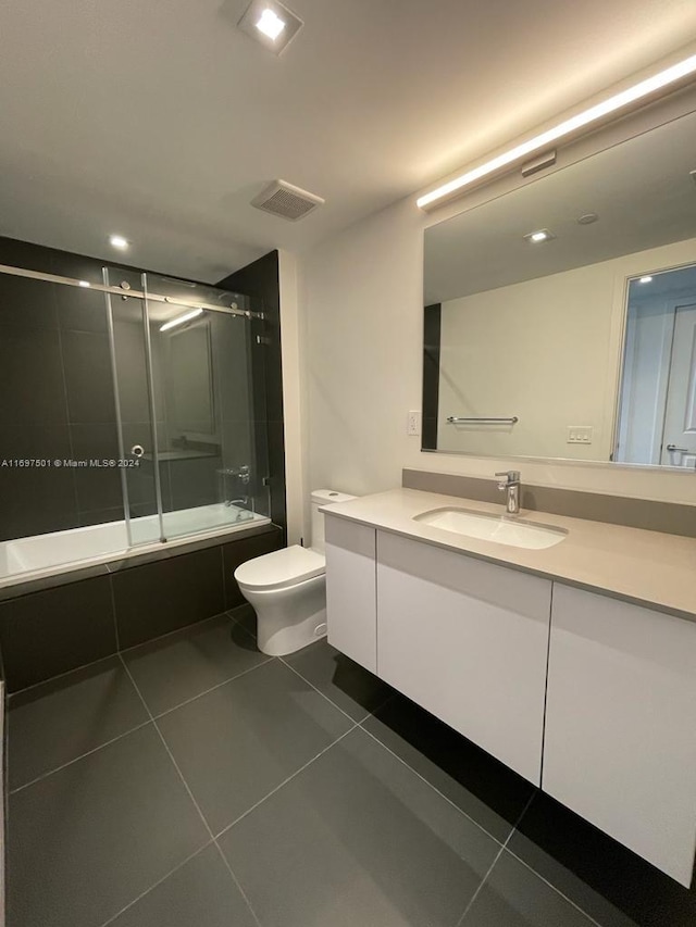 full bathroom with shower / bath combination with glass door, vanity, tile patterned flooring, and toilet