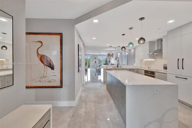 kitchen featuring wall chimney range hood, sink, hanging light fixtures, a spacious island, and light stone counters