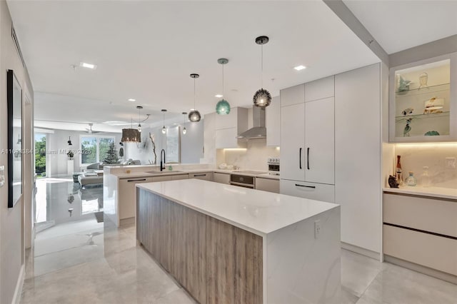 kitchen featuring wall chimney exhaust hood, hanging light fixtures, sink, and a kitchen island