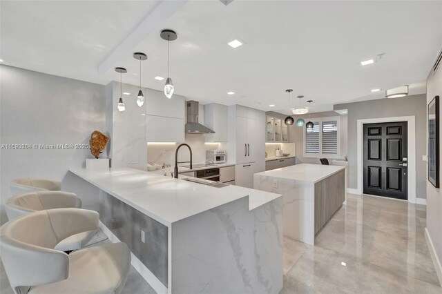 kitchen with pendant lighting, a large island, kitchen peninsula, and wall chimney exhaust hood