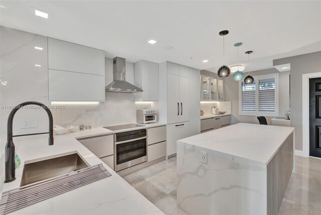 kitchen featuring decorative light fixtures, sink, oven, black electric stovetop, and wall chimney range hood