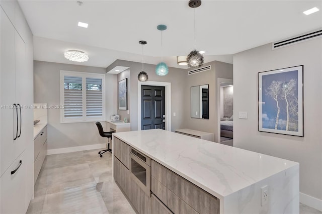 kitchen with a kitchen island, stainless steel microwave, pendant lighting, white cabinets, and light stone counters