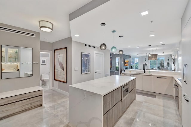 kitchen with a large island, sink, pendant lighting, stainless steel microwave, and light stone counters