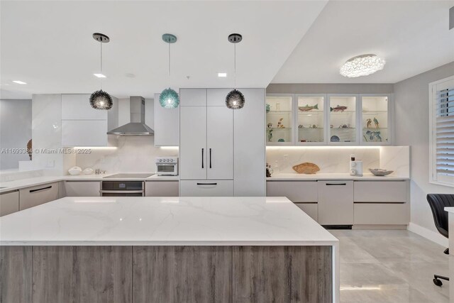 kitchen featuring pendant lighting, light stone counters, and wall chimney range hood