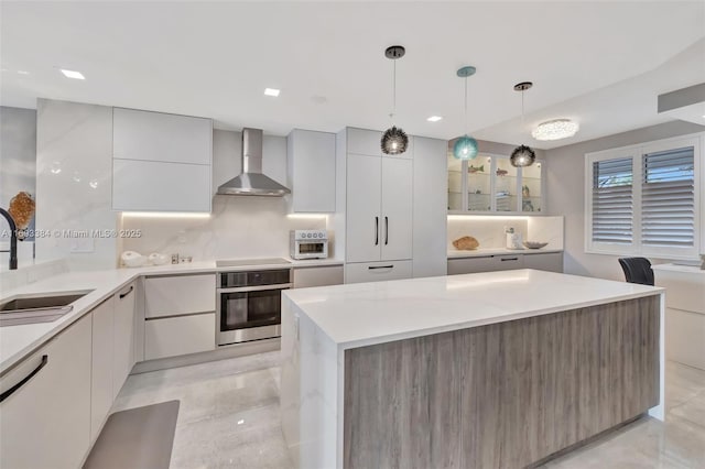 kitchen with sink, stainless steel oven, pendant lighting, decorative backsplash, and wall chimney range hood