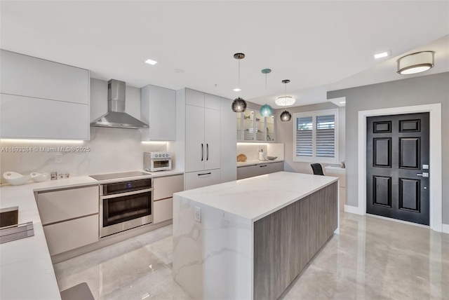 kitchen with wall chimney range hood, a center island, light stone counters, decorative light fixtures, and oven