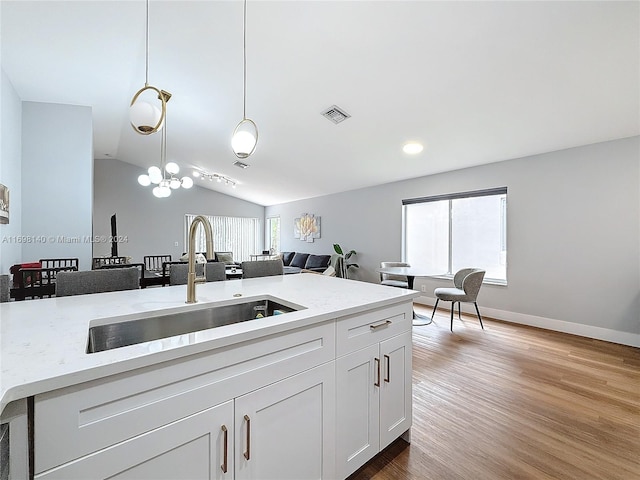 kitchen featuring white cabinetry, sink, hanging light fixtures, vaulted ceiling, and hardwood / wood-style flooring