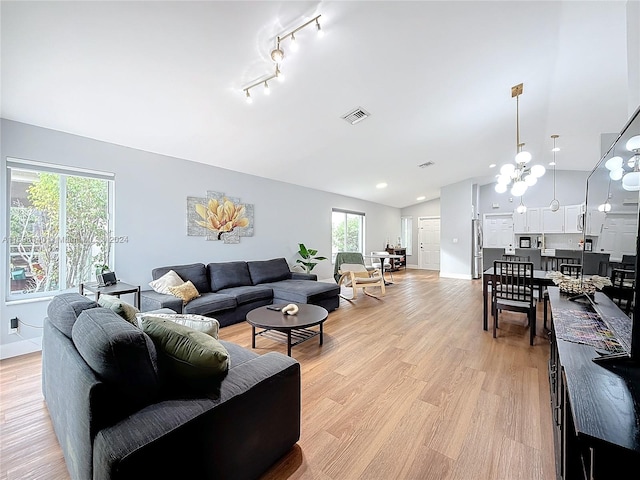 living room featuring a notable chandelier, light hardwood / wood-style floors, rail lighting, and vaulted ceiling