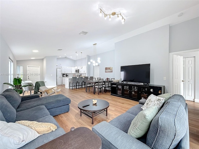 living room featuring an inviting chandelier, lofted ceiling, and light wood-type flooring