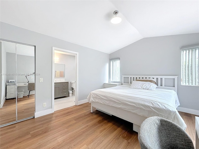 bedroom featuring lofted ceiling, ensuite bath, light wood-type flooring, and a closet