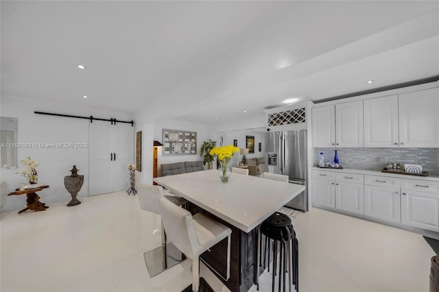 kitchen with decorative backsplash, stainless steel fridge, a kitchen breakfast bar, a barn door, and white cabinets