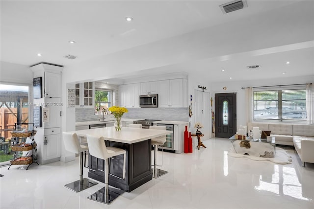 kitchen featuring wine cooler, tasteful backsplash, a kitchen island, a kitchen bar, and white cabinetry