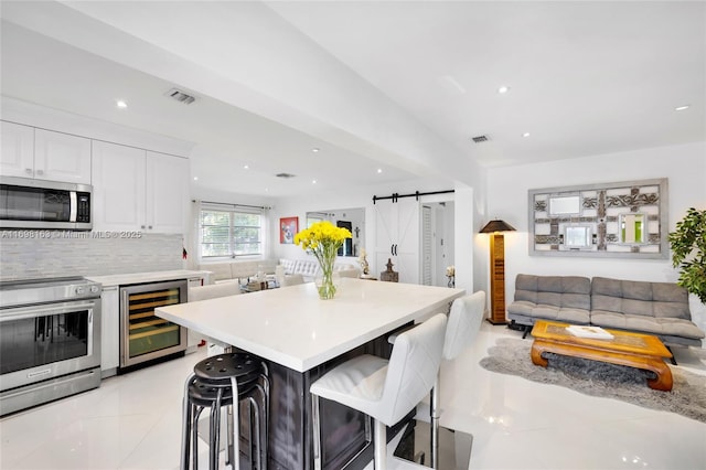 kitchen with wine cooler, a barn door, appliances with stainless steel finishes, a kitchen bar, and white cabinetry