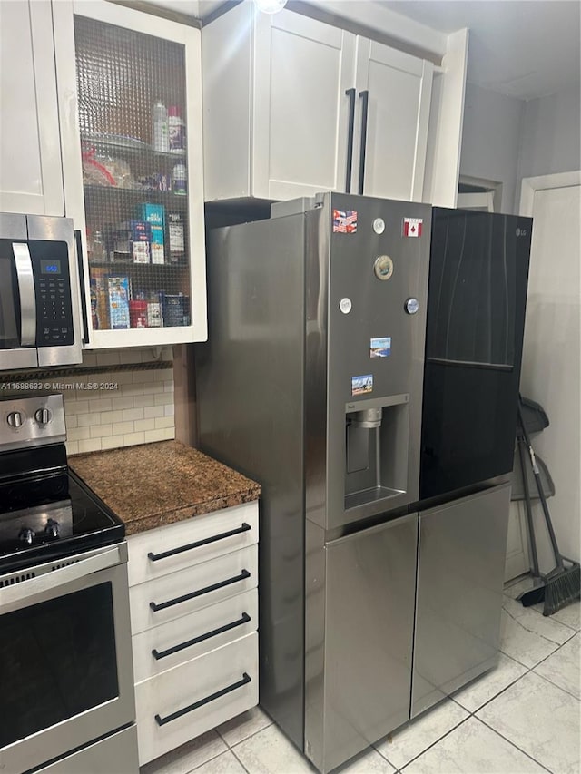 kitchen featuring light tile patterned floors, dark stone counters, decorative backsplash, white cabinets, and appliances with stainless steel finishes