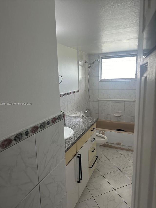 full bathroom featuring toilet, vanity, tiled shower / bath combo, and tile walls