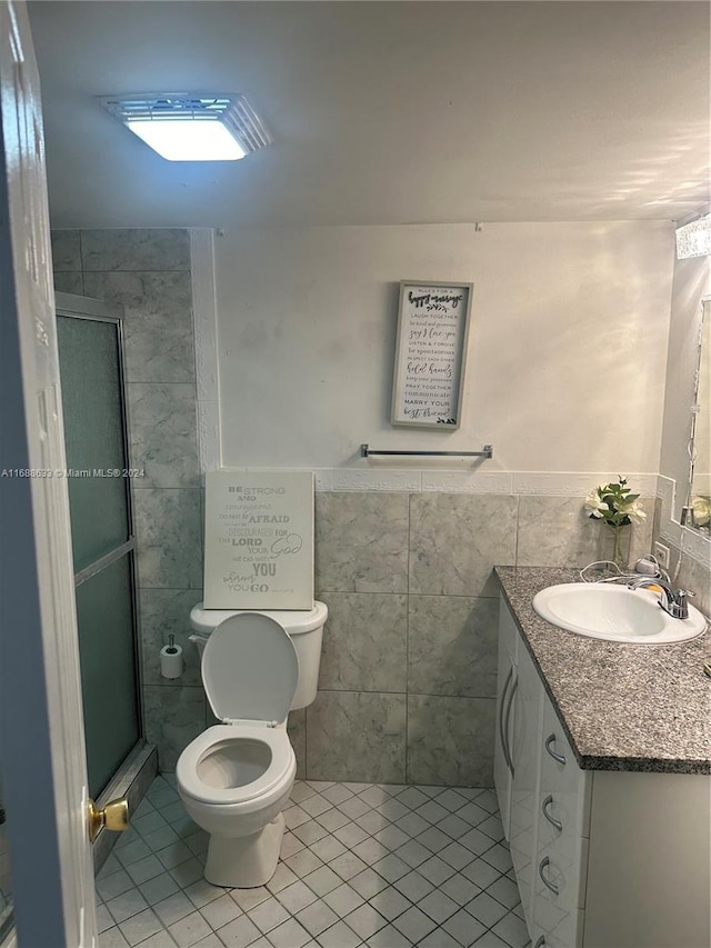 bathroom with vanity, a shower with door, tile walls, tile patterned flooring, and toilet