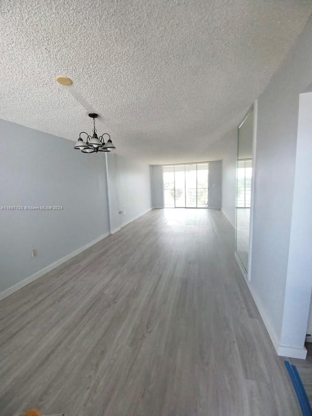 empty room with wood-type flooring, a textured ceiling, and an inviting chandelier