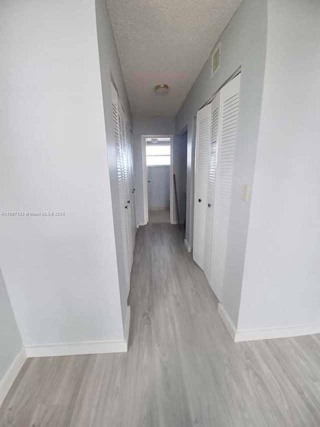 corridor featuring light hardwood / wood-style flooring and a textured ceiling