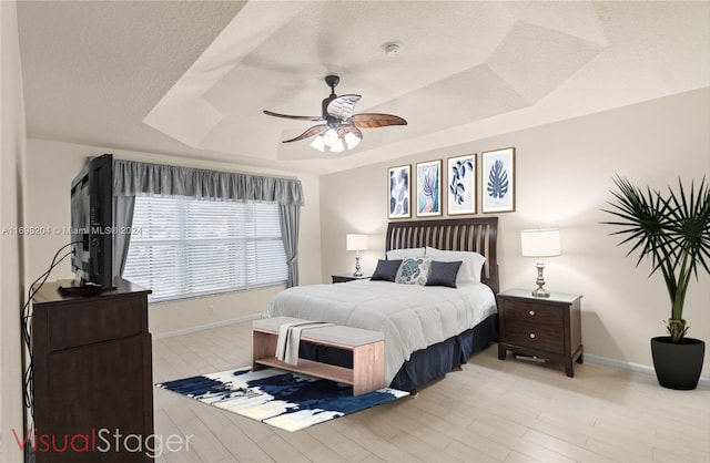 bedroom featuring ceiling fan, a raised ceiling, light wood-type flooring, and a textured ceiling