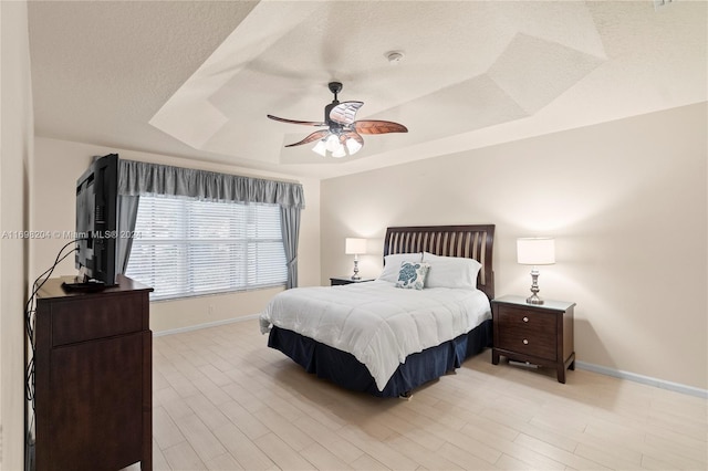 bedroom featuring a raised ceiling, ceiling fan, light hardwood / wood-style flooring, and a textured ceiling