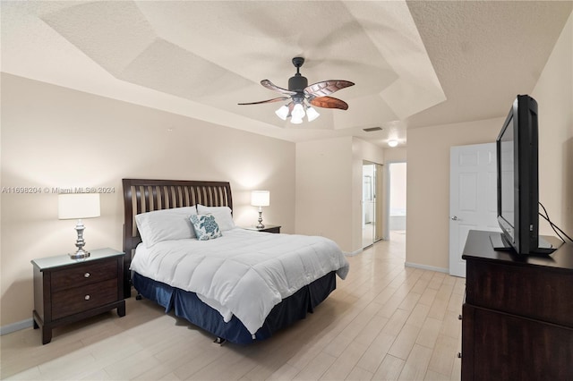 bedroom with a textured ceiling, light hardwood / wood-style flooring, a raised ceiling, and ceiling fan