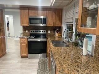 kitchen with stone counters, sink, decorative backsplash, light wood-type flooring, and stainless steel appliances