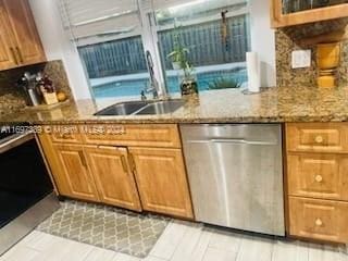 kitchen featuring dishwasher, light stone counters, and sink