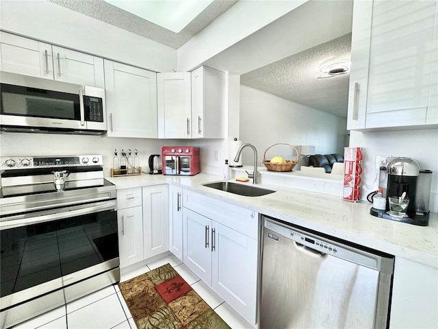 kitchen featuring a textured ceiling, stainless steel appliances, a sink, and white cabinetry