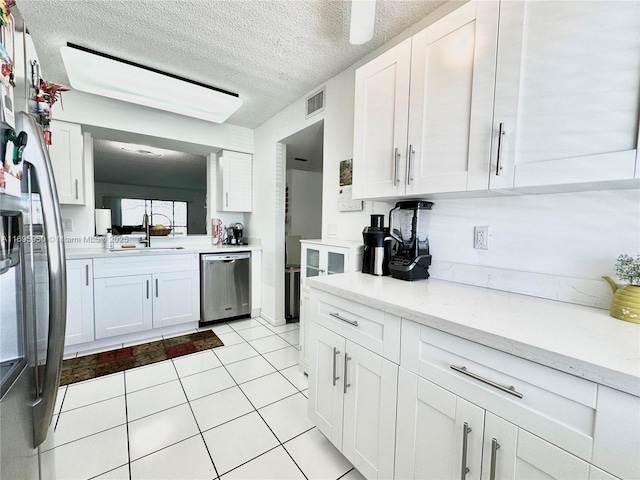 kitchen featuring appliances with stainless steel finishes, white cabinetry, a sink, and light stone countertops