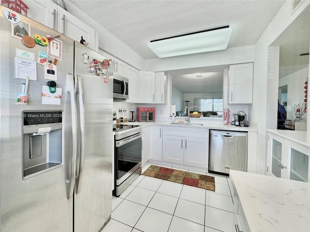 kitchen featuring light tile patterned floors, white cabinetry, appliances with stainless steel finishes, a textured ceiling, and sink